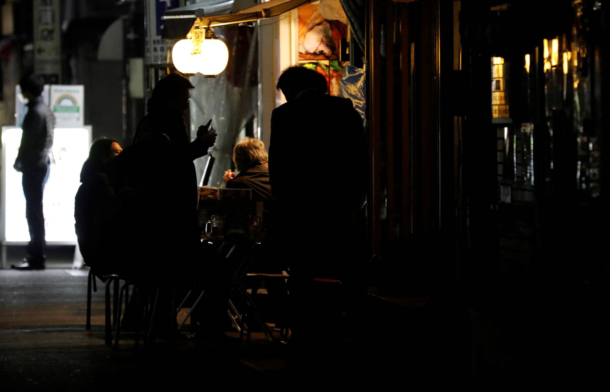 People drink by the table outside a bar that was staying open after 8 p.m., the time the government has asked restaurants and bars to close by, amid the coronavirus state of emergency in Tokyo on Friday. | REUTERS